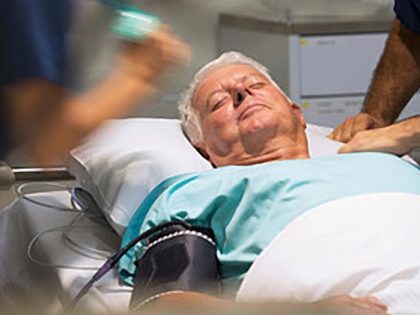 elderly male patient in green hospital gown being attended by two medics in an ICU